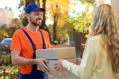 Woman receiving parcels from courier in uniform outdoors