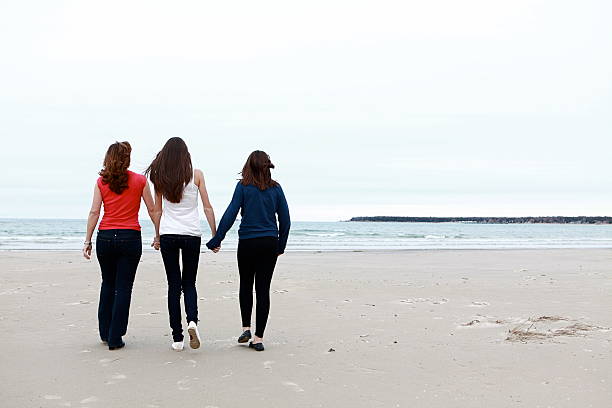 A mom and her daughters hold hands as they walk together on the beach. Copy space.