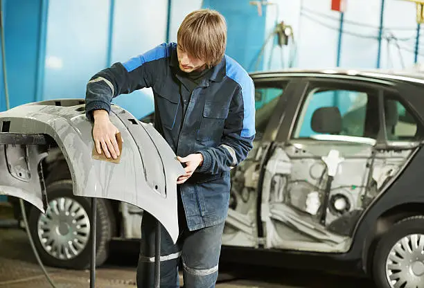professional repairman worker in automotive industry sanding plastic body car bumper