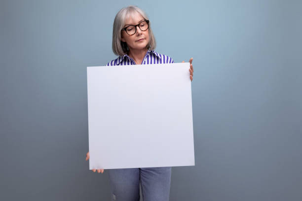 istock gray-haired mature woman showing blank sheet with mockup on bright studio background 1664410067