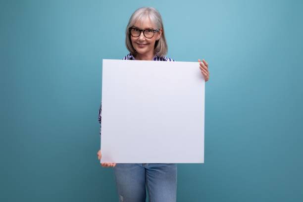 istock Successful grey-haired mature old lady shows blank billboard with mocap on bright studio background 1664410078