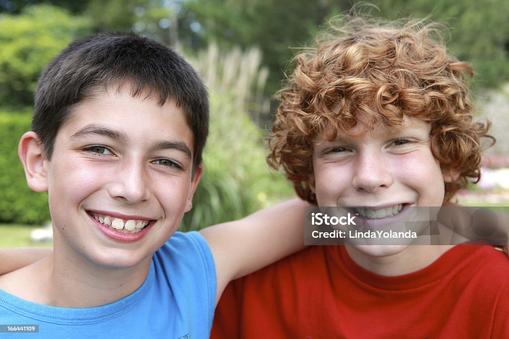 Friendship Two boys smile at the camera as they sit side by side with their arms slung across each other's shoulders. Sharpest focus on boy on left. Friendship Stock Photo