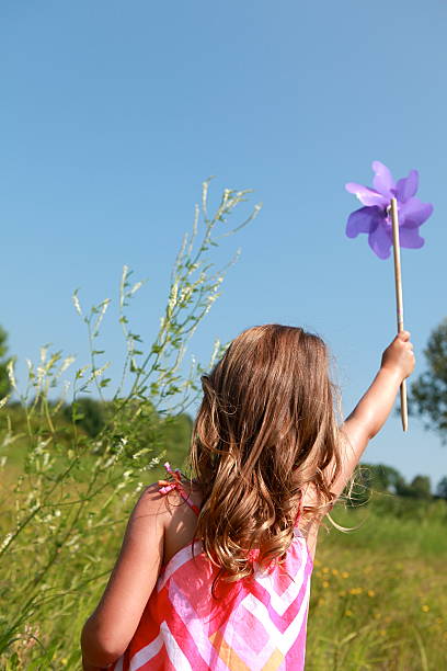 A little girl holds a pinwheel up against a blue sky. Copy space.
