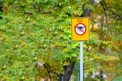 Prohibiting yellow square sign no fly zone drone against background of trees, public park. Safety of tourists, secret object, protected area Aircraft restriction in national parks, untouched nature