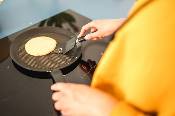 An unrecognizable woman making American pancakes for a family breakfast at home.