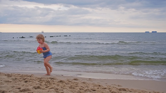 Cute Little Caucasian Toddler Girl Wearing Swimsuit Playing on Beach Running Away Scared by Sea Waves Breaking on Seashore