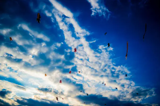 A swarm of colorful kites set against a cloudy blue sky at Mertasari Beach in Sanur, Bali, Indonesia.