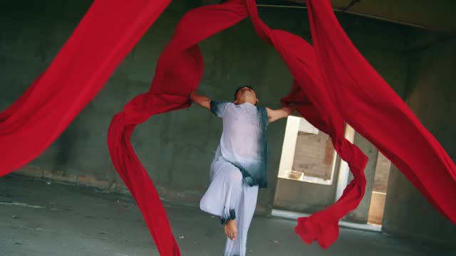 an Asian man dancing with a hanging red cloth very agile and energetic in an old building