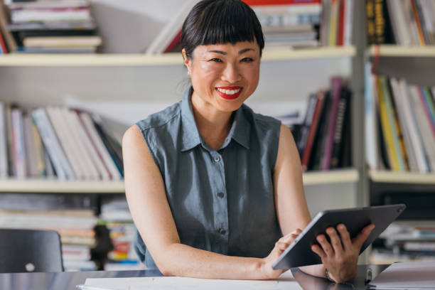 istock A Happy Beautiful Asian Businesswoman Looking At Camera While Working On Her Tablet 1664545019