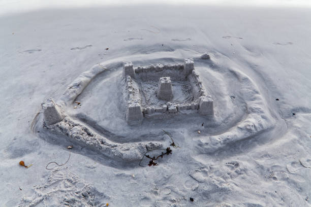 istock Sand Castle On Beach Eroded By Returning Water With Foot Prints 1664547265