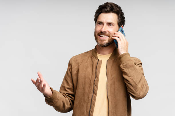 istock Handsome smiling bearded man in leather jacket, gesturing while talking on mobile phone 1664568641
