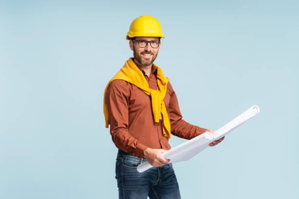 istock Smiling architect or engineer wearing yellow hard hat holding architectural drawing 1664569256