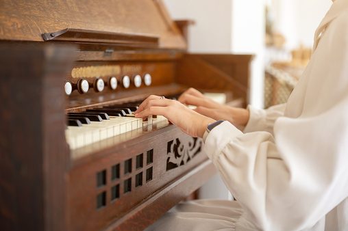 Close-up image of a talented woman in a cute white dress playing a classic piano in her living room. People and music instrument concepts