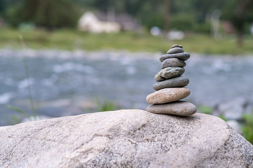 A pyramid of bare stones stacked on top of each other. Stones stacked in the shape of a pyramid on the riverbank against the background of mountains as balance and balance in nature, Zen, Buddhism.