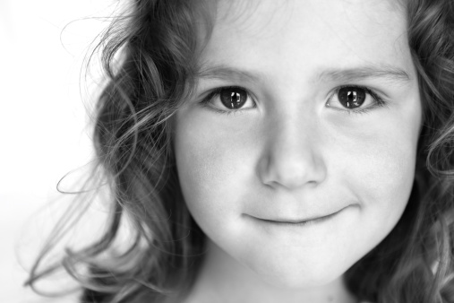 A close up portrait of an adorable 4 year old girl with a sweet smile. Black and white portrait on a white background.