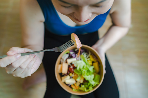 Woman in exercise clothes eating alternative food, fruit and vegetable salad, diet concept for weight control and good health.