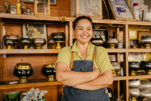 A smiling handicraft shop owner with crossed arms takes pride in her small business in Thailand