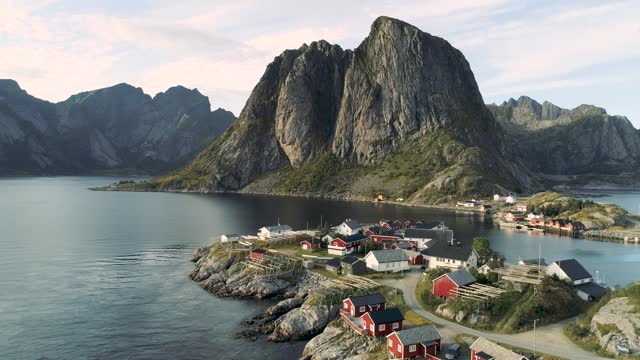 Aerial footage of red houses hanging over the ocean from a small island Hamnoy -Reine- in Lofoten archipelago, northern Norway, with dramatic mountains in the background
