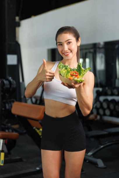 카메라에 그릇에 담긴 야채를 보여주는 아름다운 아시아 여성 - eating body building muscular build vegetable 뉴스 사진 이미지