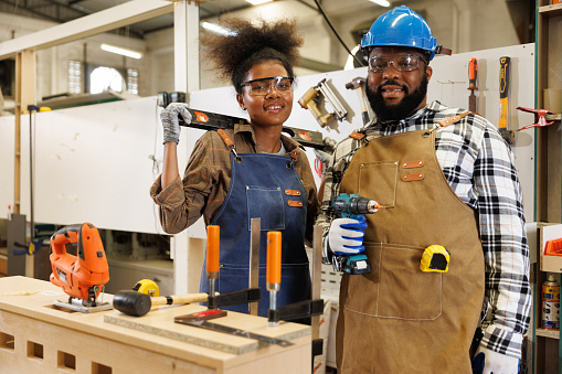 Portrait young woman and black man carpenter holding the tools in factory