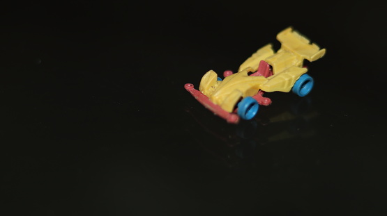 A miniature toy race car in yellow, blue and red color combination on a Black shiny surface in isolated black background