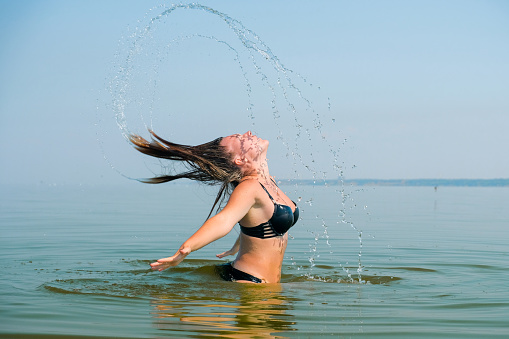 A beautiful girl in a bathing suit splashes water with her hair into the sea. Frozen movement.
