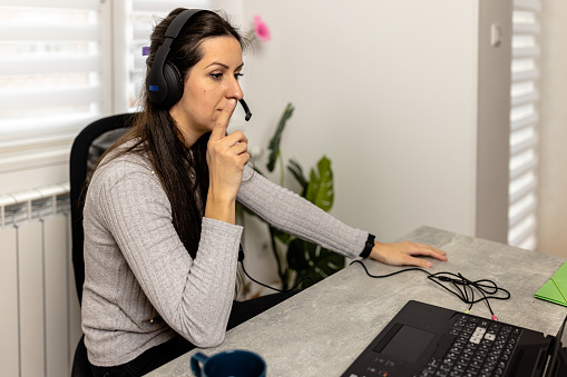 A woman with headphones and a microphone is consulting clients on the phone in customer support service, looking at a computer screen.