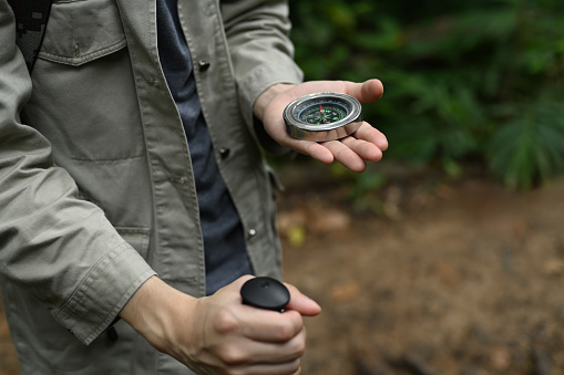 Male hiker using compass for directions in the forest, enjoying his active vacation.