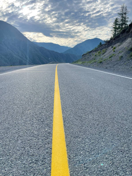 istock Asphalt road with yellow line in the mountains under cloudy sky. 1665032222
