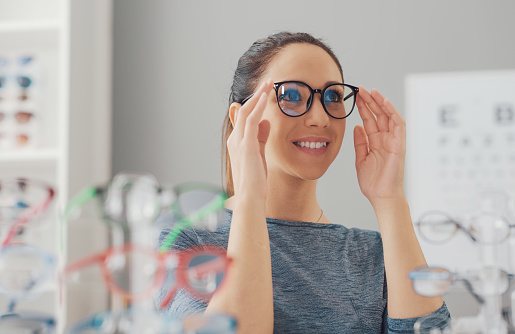 Young smiling woman choosing a new pair of prescription glasses at the eyewear store