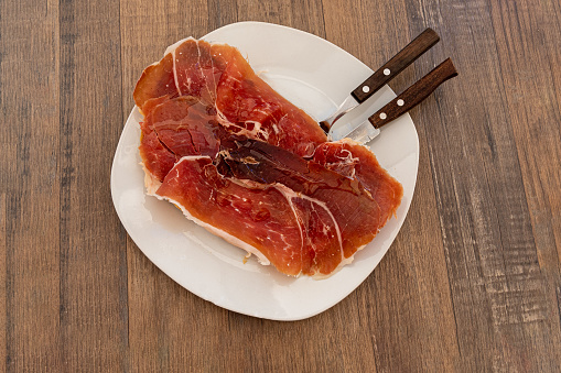 A plate of Iberian ham with olive oil on toasted bread, breakfast snack, typical Spanish snack. On a wooden table. Ready to eat. Slice of iberian pork ham to accompany breakfast.