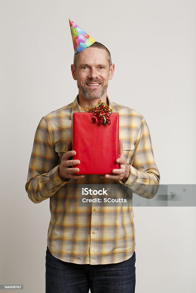 Uomo in Cappello partito tenendo il regalo e sorridente - Foto stock royalty-free di Abbigliamento casual