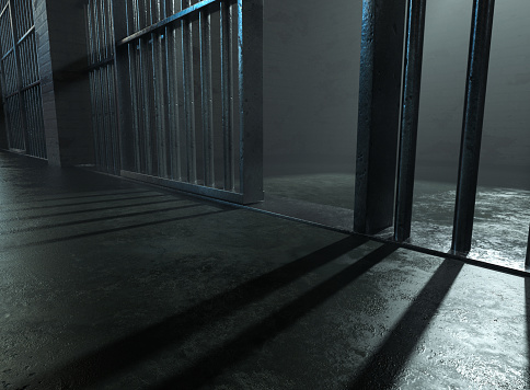 A closeup of a spolight behind jail cells iron bars casting shadows on the concrete prison floor - 3D render