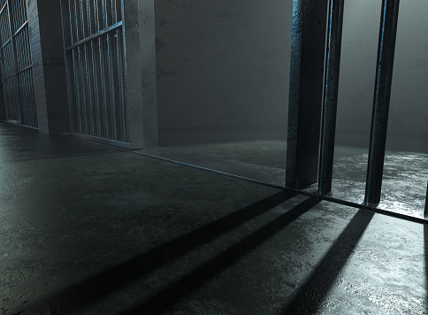 A closeup of a spolight behind jail cells iron bars casting shadows on the concrete prison floor - 3D render