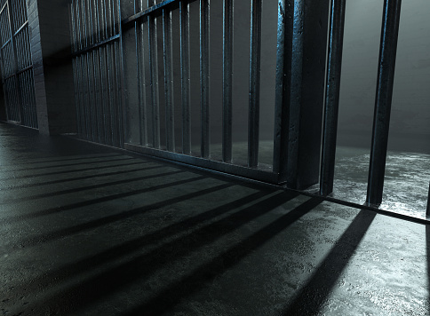 A closeup of a spolight behind jail cells iron bars casting shadows on the concrete prison floor - 3D render