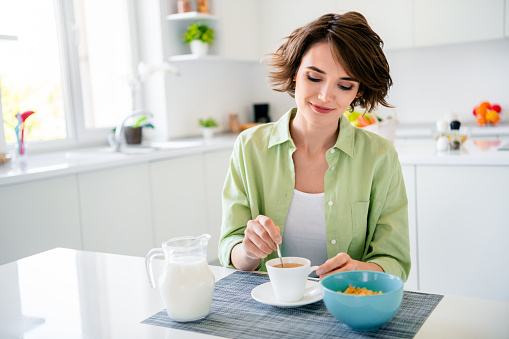 Photo of cute sweet girl wear green shirt enjoying fresh coffee eating breakfast indoors kitchen room.