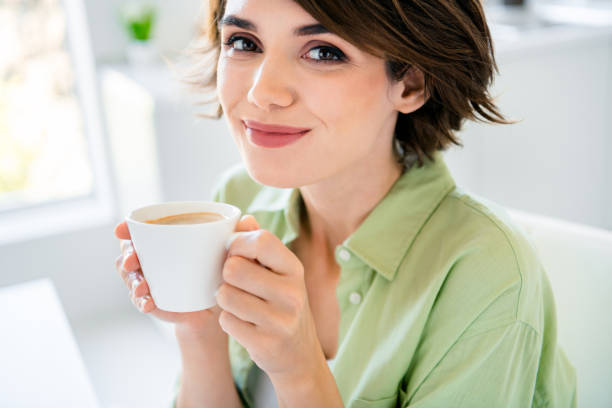 꿈꾸는 흥분된 소녀가 녹색 셔츠를 입고 실내 주방 방에서 신선한 에스프레소 커피 음료를 즐기는 사진 - stereotypical housewife women domestic kitchen brown hair 뉴스 사진 이미지