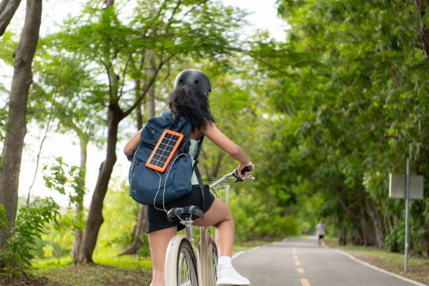 Rear view of Asian woman riding a bicycle in the park. It has a backpack with a solar panel for charging smartphone.