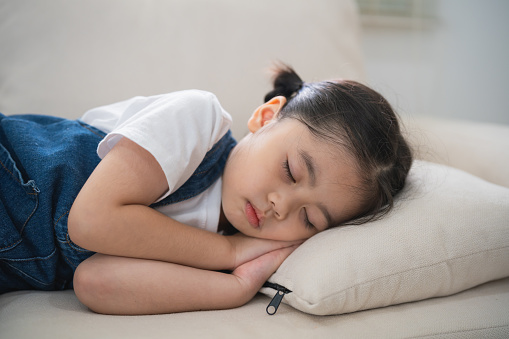 Cute little girl child sleeping on couch sofa with soft pillows at living room at home. Baby girl lying on the sofa couch bed.
