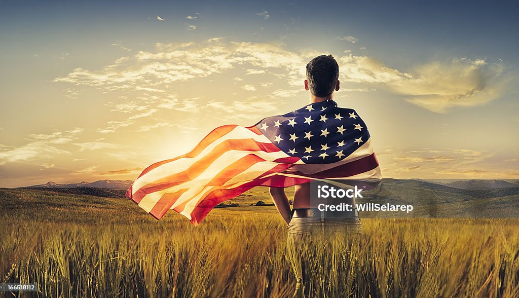 Giovane uomo avvolto bandiera americana campo coltivato tramonto - Foto stock royalty-free di Bandiera degli Stati Uniti