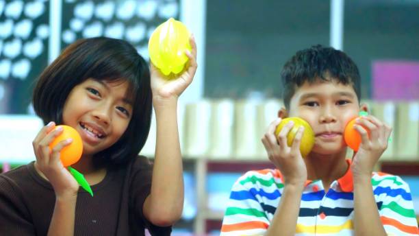 Asian students having  playing with toy fruits and vegetables.