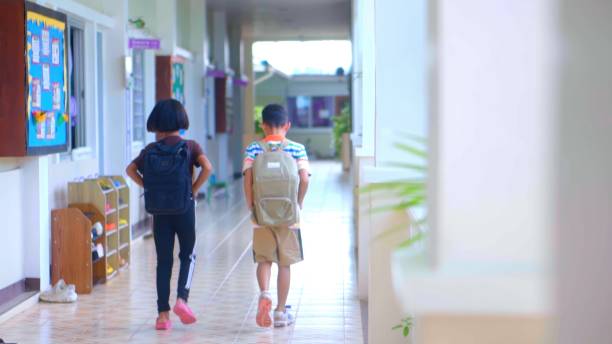 istock Rear view of pupils asian rushing down school corridor. 1665187375