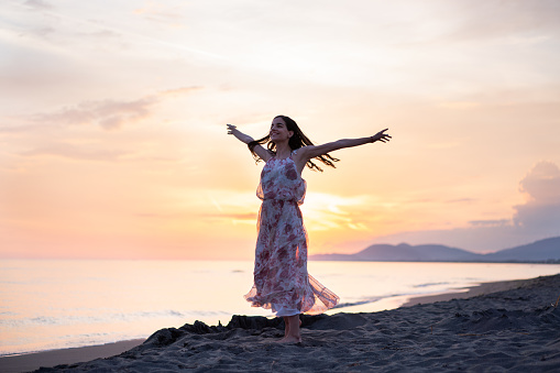 Woman whit outstretched hands standing at the beach during sunset