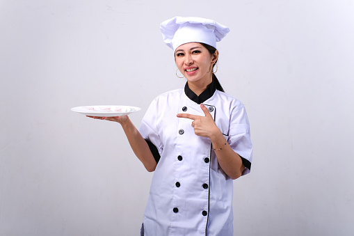 Smiling female Asian chef holding empty plate isolated on white background