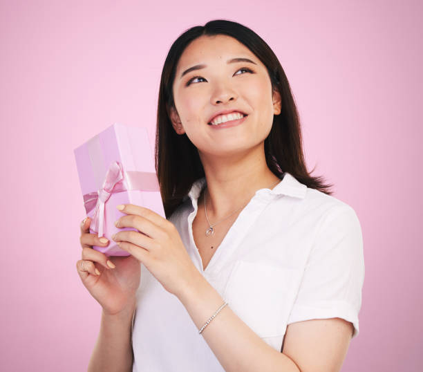 istock Gift, thinking and Asian woman giving present box happy for celebration isolated in a studio pink background. Giveaway, ribbon and person with happiness for surprise or prize package with smile 1665220429