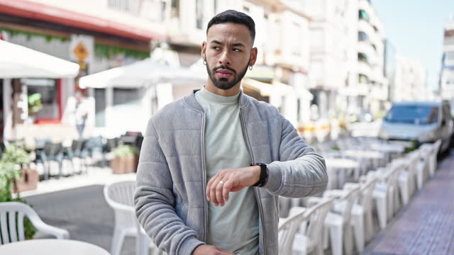 Young hispanic man with serious face looking watch at street