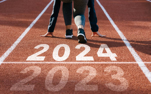 ein frohes neues jahr 2024 symbolisiert den beginn des neuen jahres. rückansicht eines mannes, der sich darauf vorbereitet, auf der leichtathletikbahn zu laufen, in die das jahr 2024 eingraviert ist. das ziel des erfolgs.sich auf das neue jahr vorbereiten - track event running competition sports race stock-fotos und bilder