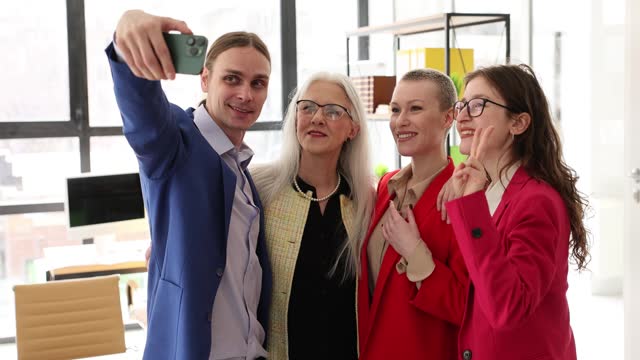 Happy business team of company are having fun at workplace looking at screen of smartphone taking selfie