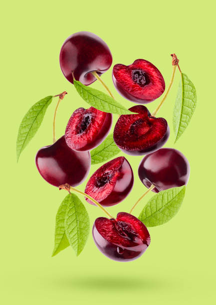 istock Bright red cherry with green leaves closeup levitation as flow, art composition. Whole, half fruits on bright green background, shadow. Summer ripe fruits for advertising, design, label product, card. 1665273961