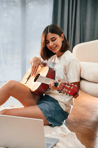 Learning to play classical guitar. Beautiful woman in casual clothes is at home in domestic room.